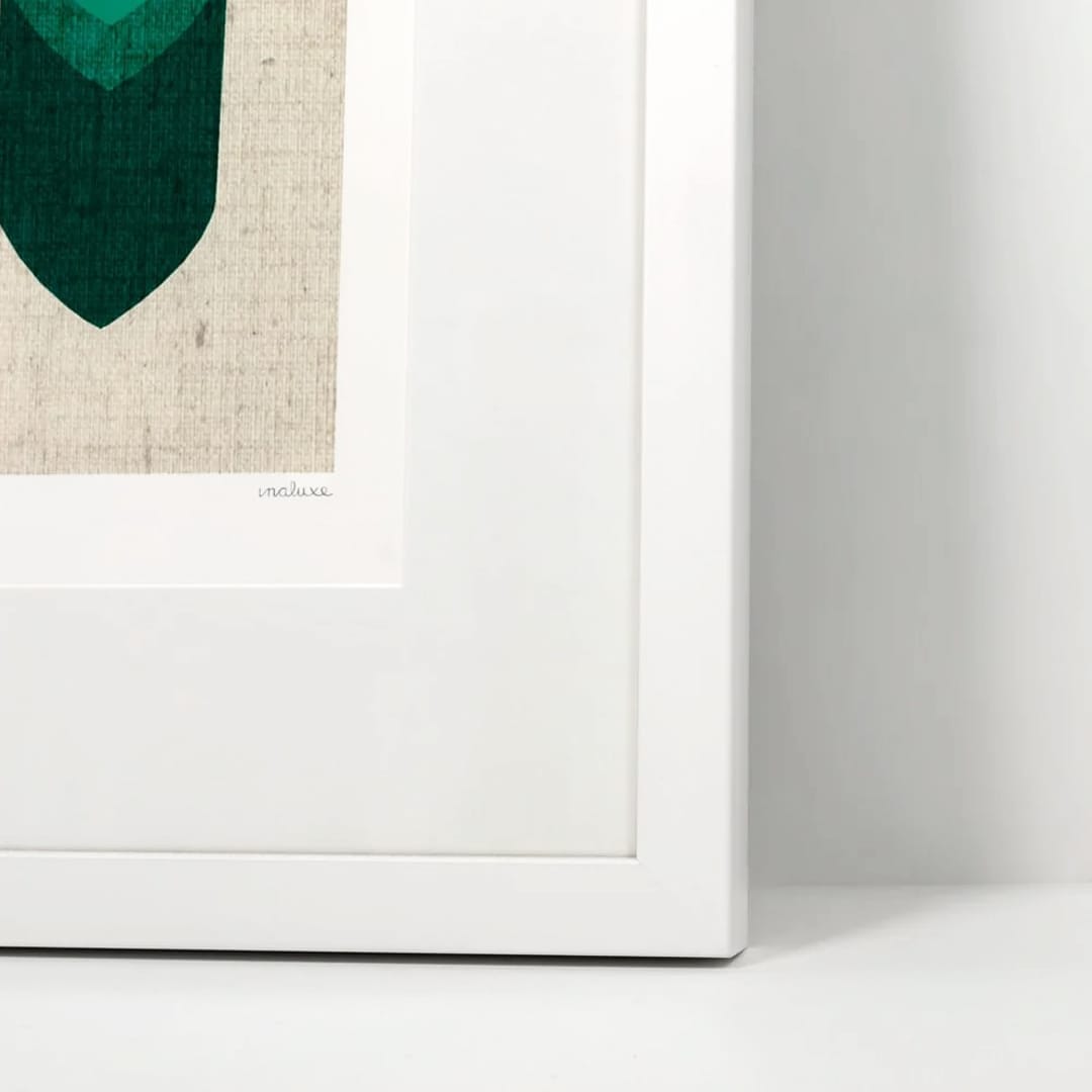 A close-up of a framed art print showing a white frame, white mat, and part of a geometric design in dark green and teal on a textured beige background.