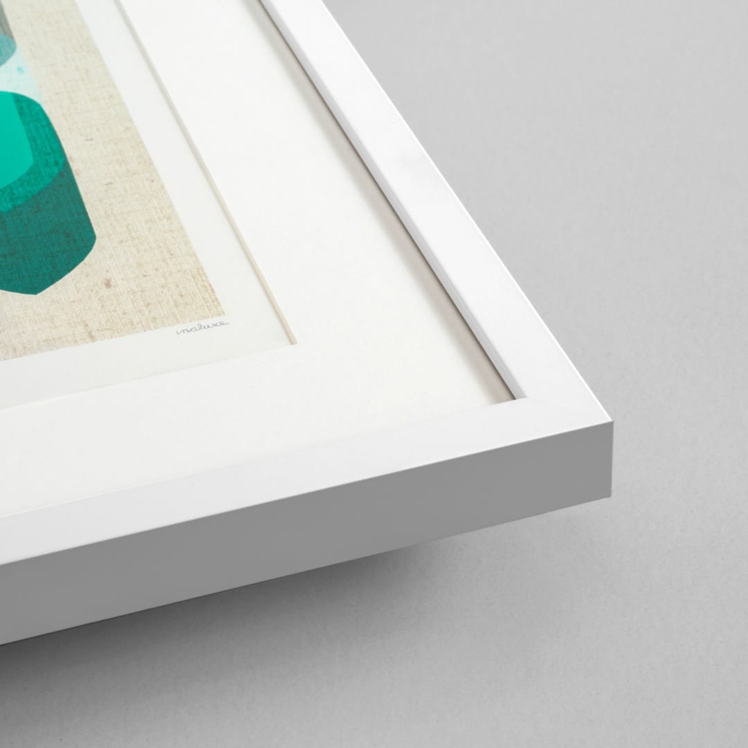 Close-up of a white square picture frame with a white mat, showing part of a colorful art print with a teal geometric shape on a beige textured background, set against a light gray wall.
