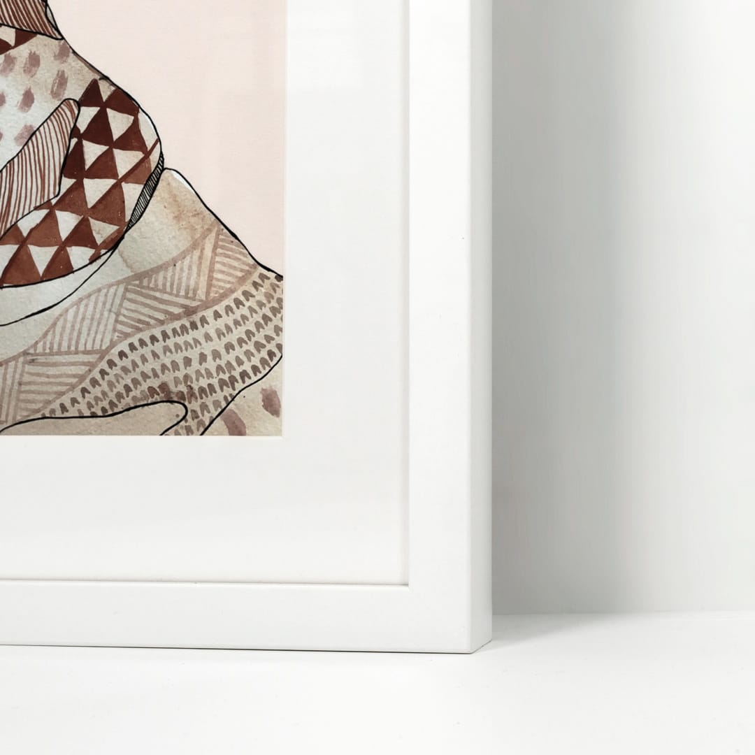 A close-up of a framed art print showing a stylized patterned illustration in brown, beige, and cream tones against a pale pink background, set in a clean white frame on a white surface.