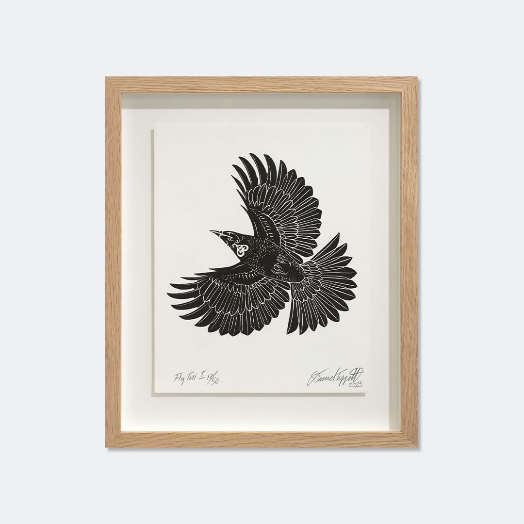 A framed black and white art print of a flying tui, featuring a light oak wood frame and a cream mat border, displayed against a neutral light gray background.