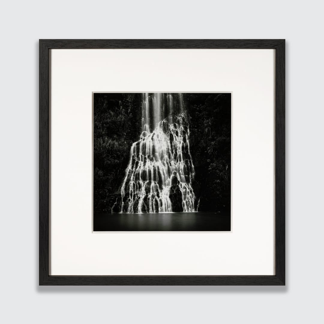 Framed black and white photographic print of Karekare Falls waterfall, featuring a white mat board and a sleek black custom frame